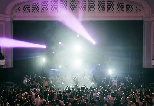 Large indoor concert hall with stage lighting and audience